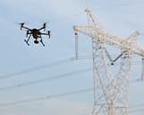 Luftaufnahme einer Drohne vor einer Stromleitung mit blauem Himmel im Hintergrund