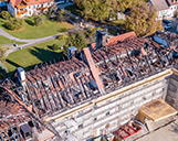 Luftaufnahme von einem großen Haus aus der Entfernung mit abgebranntem Dach