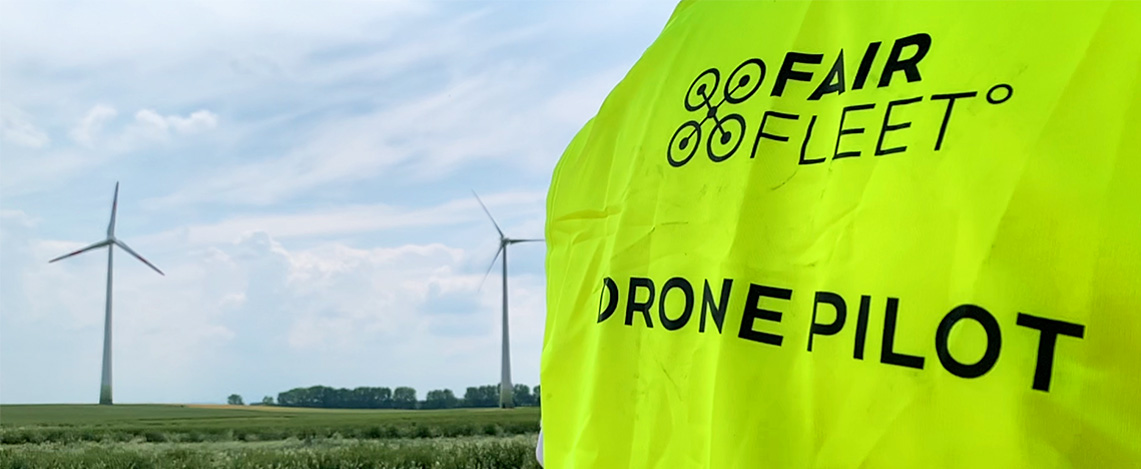 Drohnenpilot mit gelber Warnweste vor einem Windrad